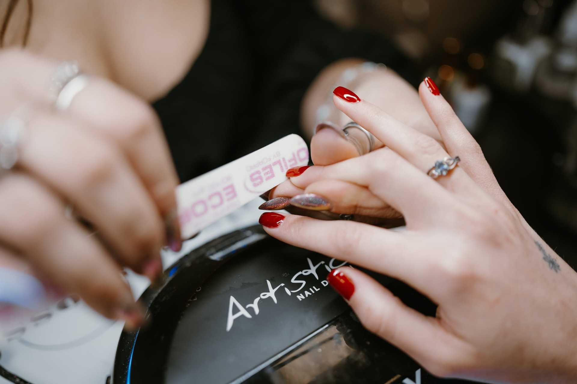 Nail technician filing red-painted nails in a salon.