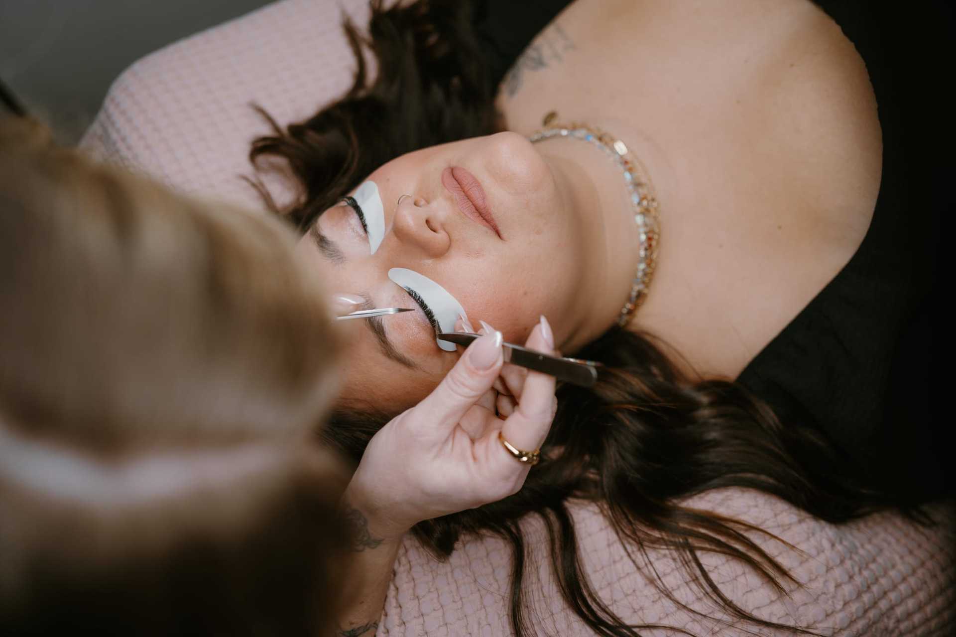 Woman receiving eyelash extension treatment from a beautician.