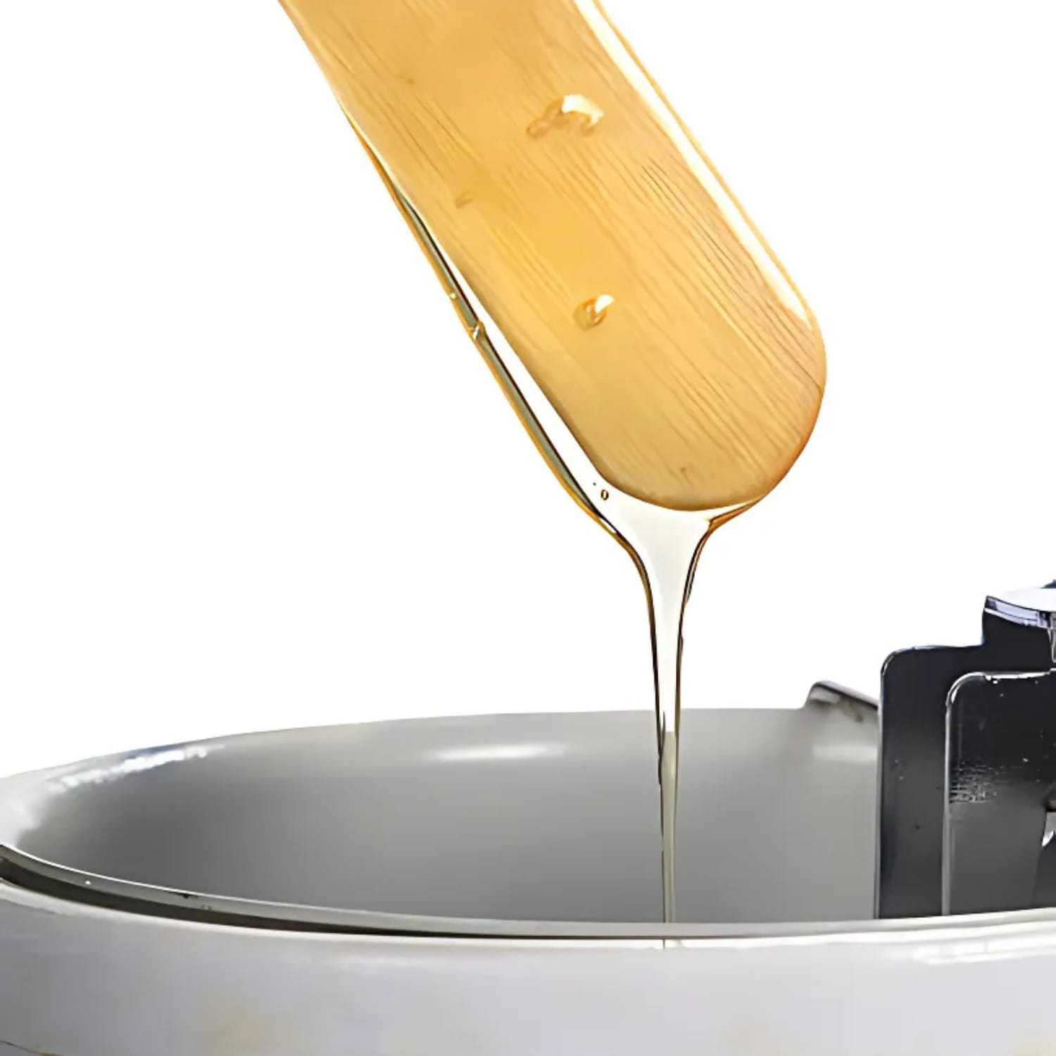 Wax dripping from a wooden spatula into a warmer on a white background.